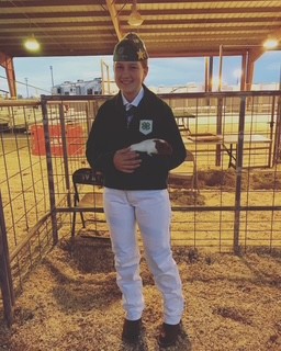 Addison Holbrook holding a cavy in a livestock pen during a 4-H small animal show. Addison is wearing white pants, a green 4-H Branded waist length jacket and the California 4-H Hat. 