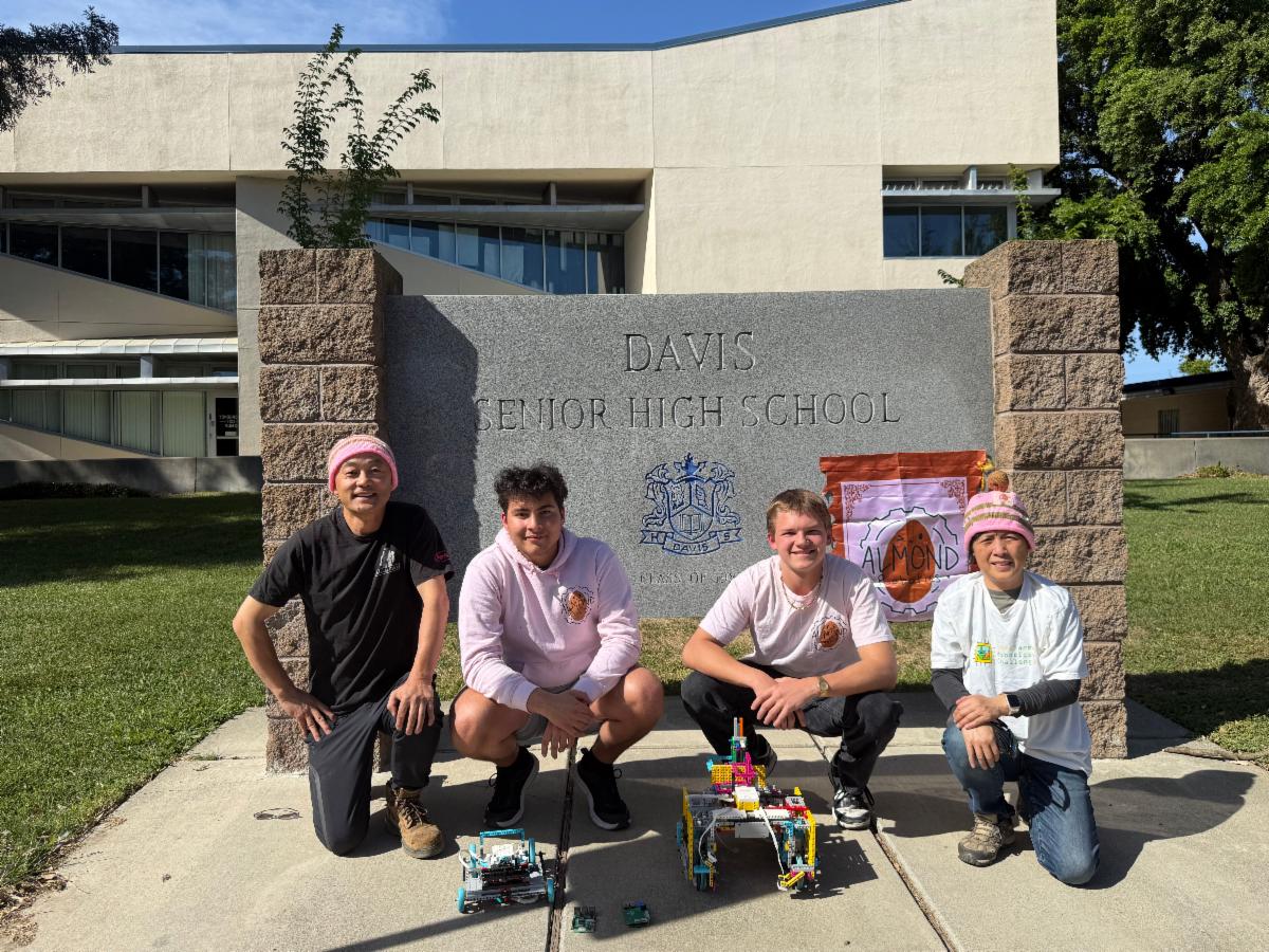 Almond Robotics team kneels in front of Davis Senior High School sign with their robots in front of them.