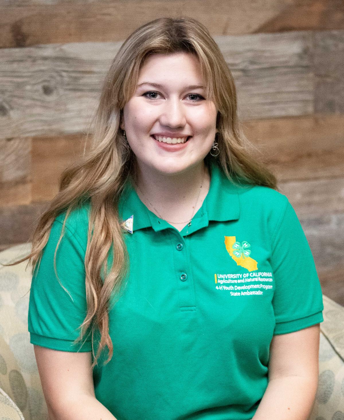 Addison Holbrook as in her State Ambassador year 2022-2023. Addison sitting, smiling, wearing the State Ambassador Green Polo shirt and State Ambassador pin on the collar.