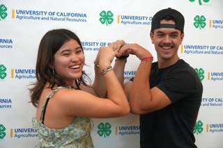 Two smiling youth participants pose back-to-back and flex their arms in front of a University of California Agriculture and Natural Resources and 4-H step-and-repeat backdrop.