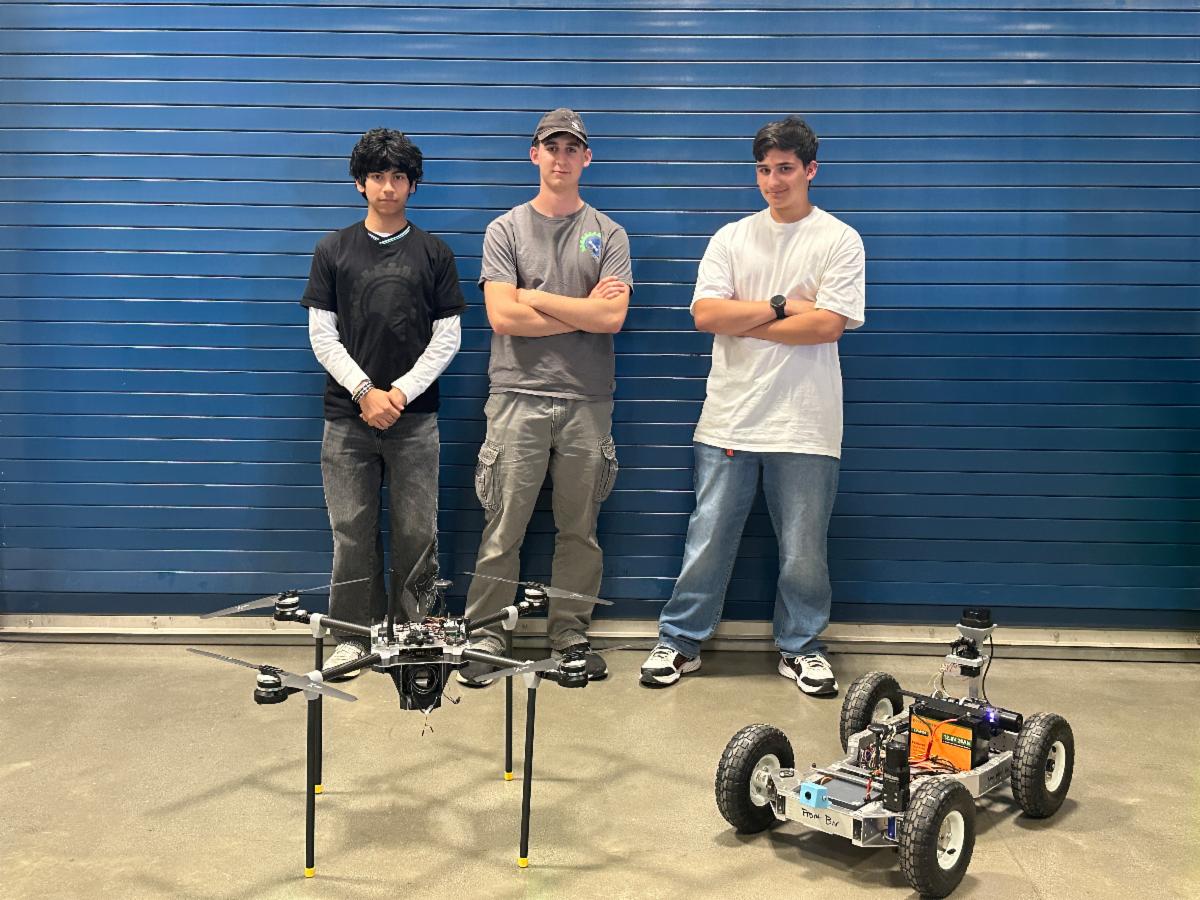 3 CTEC students stand together with their drone and robot in front.