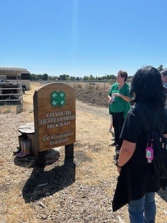  Ms. Susan Weaver, Regional Program Coordinator stands at the 4-H Youth Development Program sign at Homesteaders 4-H Ranch.