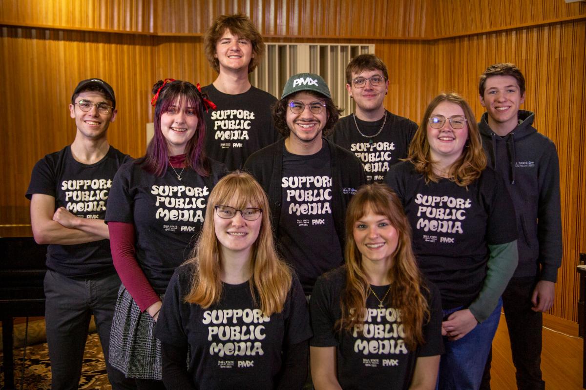 A group of young adults wearing matching black t-shirts posed in a room with wood paneled walls