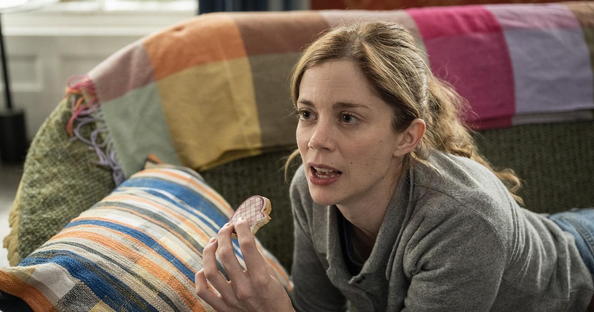 A woman is propped up on a couch holding a decorative cookie while talking to someone off-camera