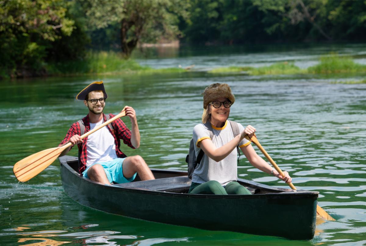 Photo illustration of a man and a woman rowing a canoe on a river, the woman is wearing a fur hat and the man is wearing a tricorn hat