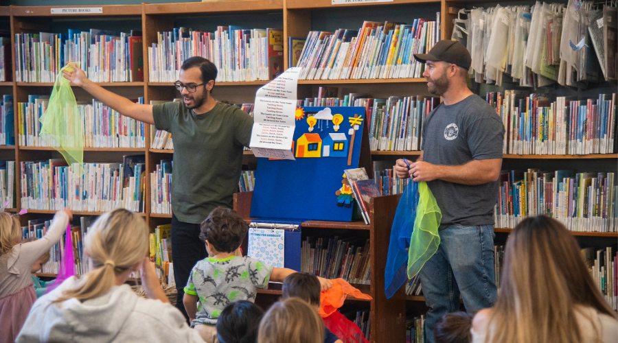 Two PWP employees lead a story time for kids in front of shelves full of books.