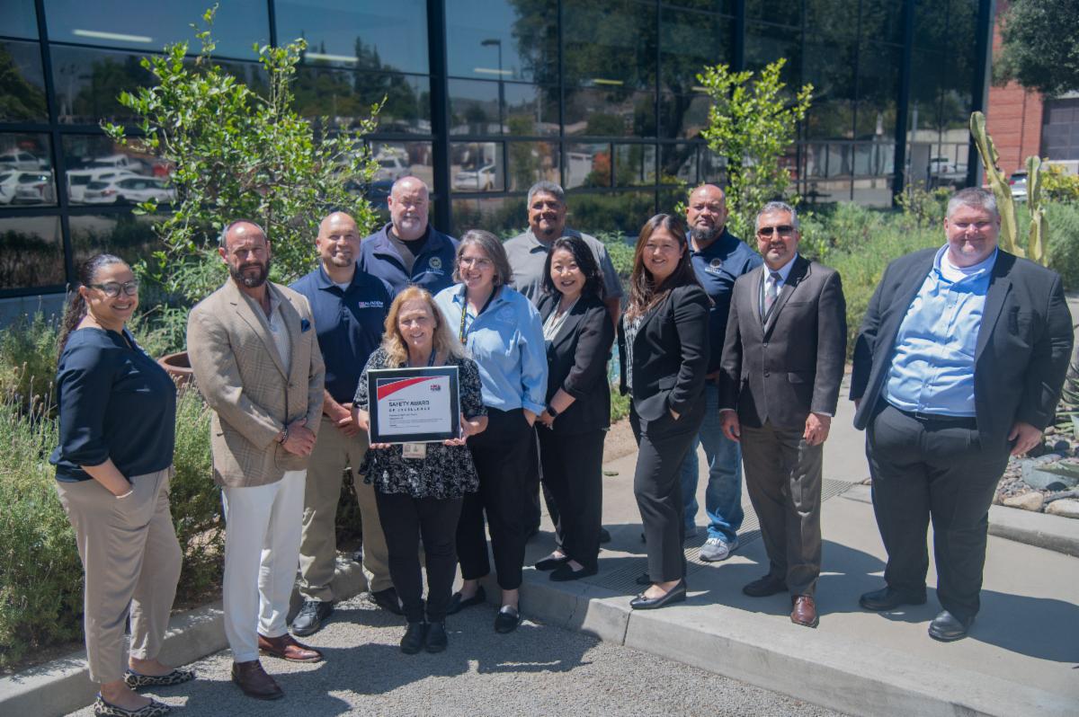 PWP employees stand in a group outdoors in daylight holding a safety award plaque.