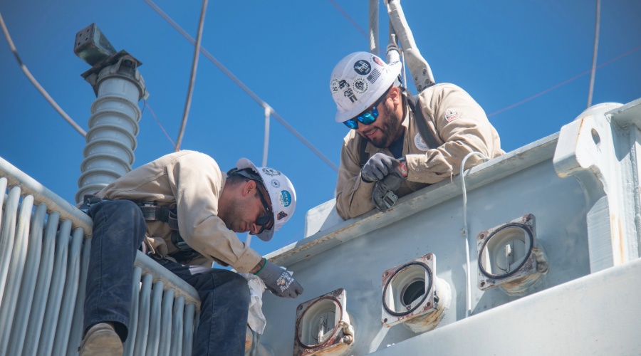 Two linemen seen from below work at the TM Goodrich receiving station.