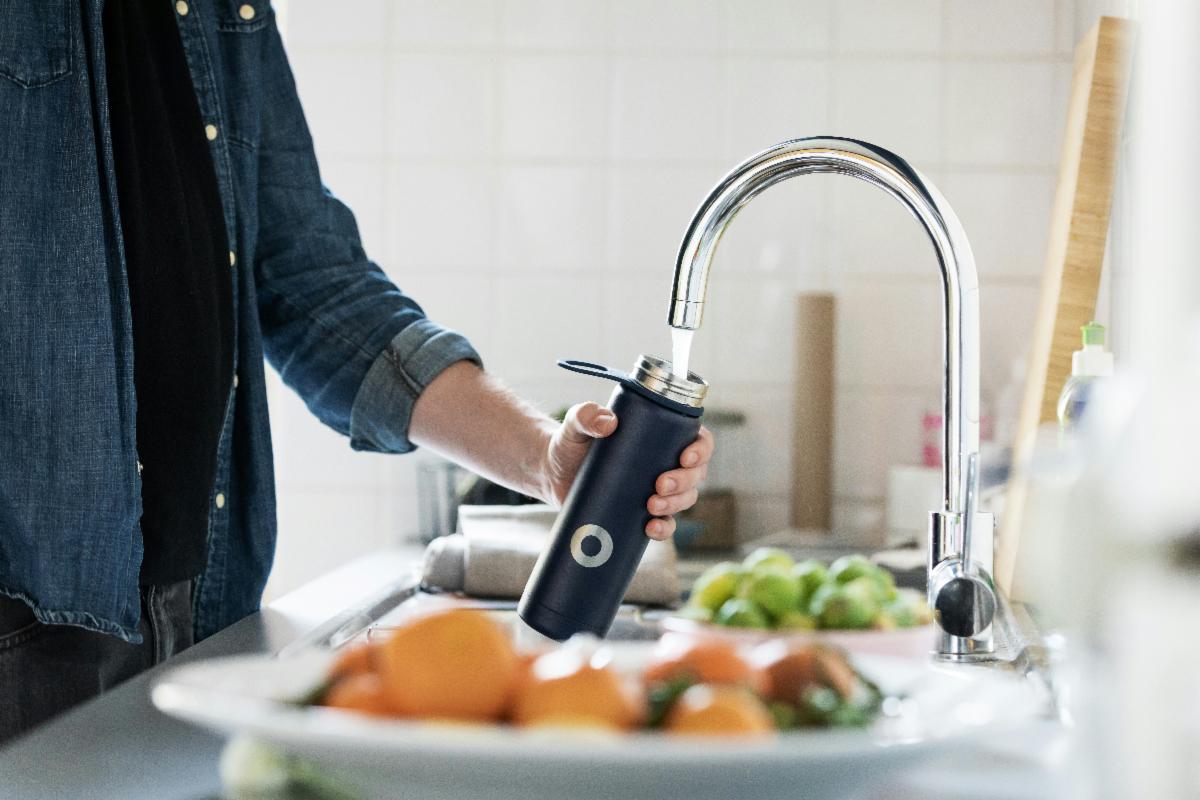A man filling a water bottle in a kitchen sink