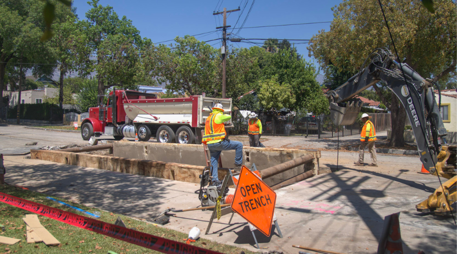 Crew members in orange safety vests install an underground vault on Raymond Avenue.