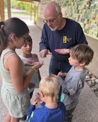Rick Simek leans over students huddled around looking at seed pods. Kids show engagement and interest.