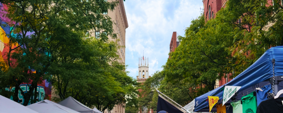 Manchester City Hall clock tower behind trees and tents at a street fair