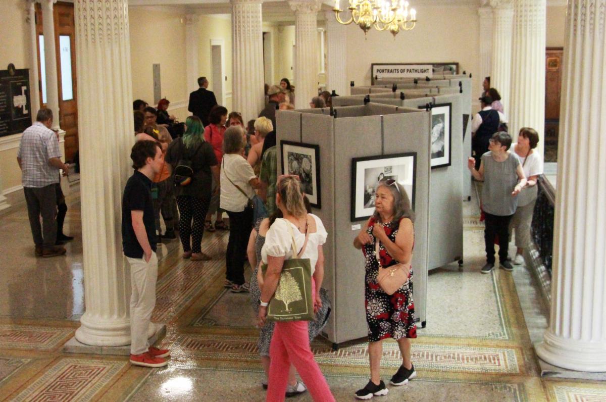 Pathlight supporters walk around the Portraits of Pathlight photography exhibit at the Boston State House, 4th floor. The exhibit features black and white photos of people with disabilities.