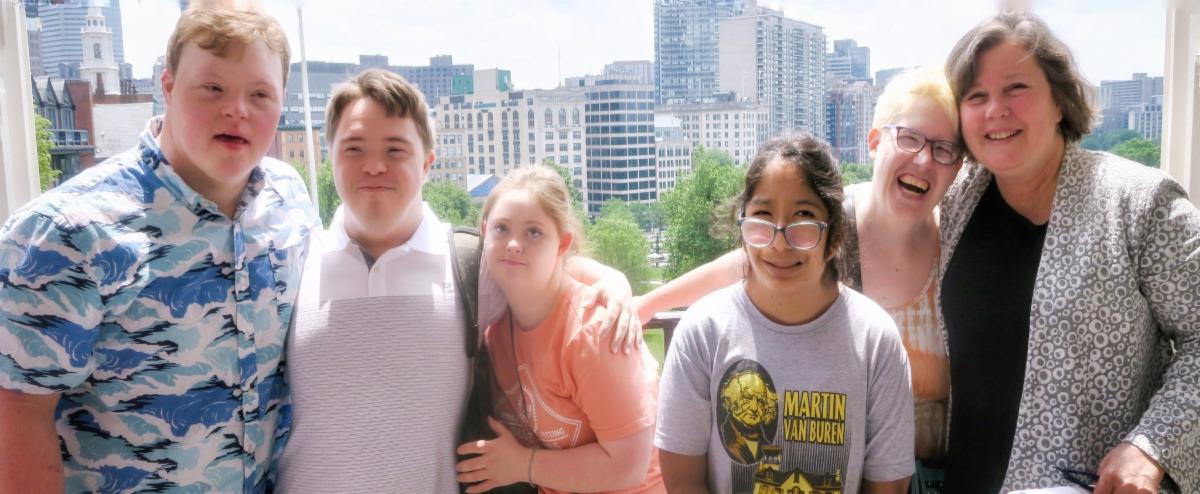 group photo of 5 Whole Children and Milestones students with Senator Jo Comerford on the Boston State House balcony with skyscrapers in background