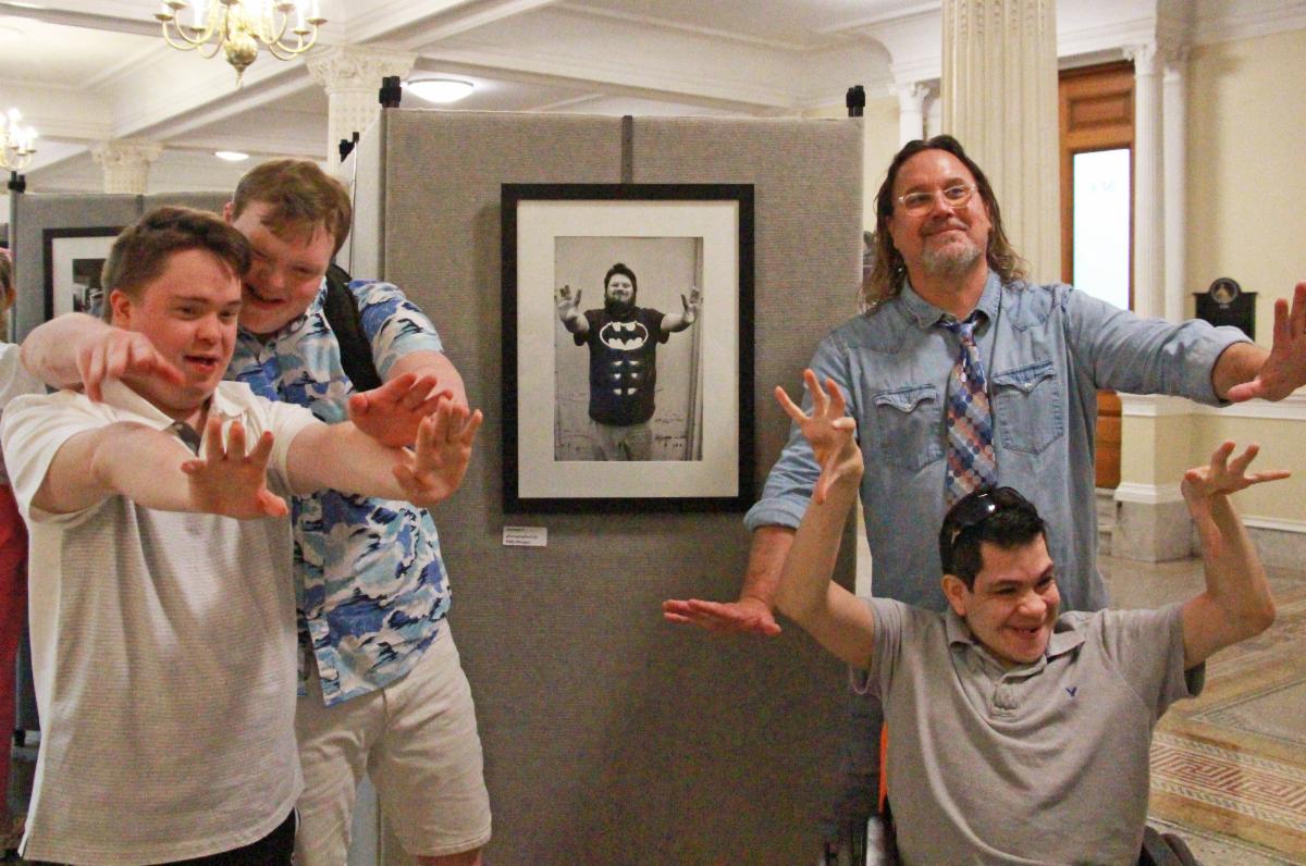Members of Milestones' Men's Group stand in front of Jeremy's portrait at the Boston State House, holding their arms out like Jeremy does in his portrait