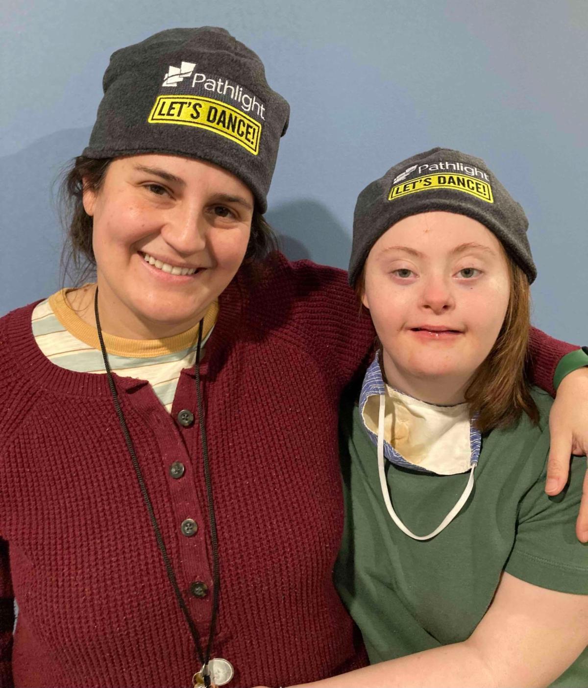 Milestones Program Manager with a student, both wearing gray hats with white and yellow text that says "Pathlight- Let's Dance!"