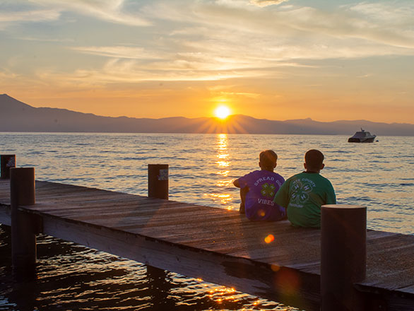 Two 4-H participants watch a sun set while sitting on a dock in Lake Tahoe