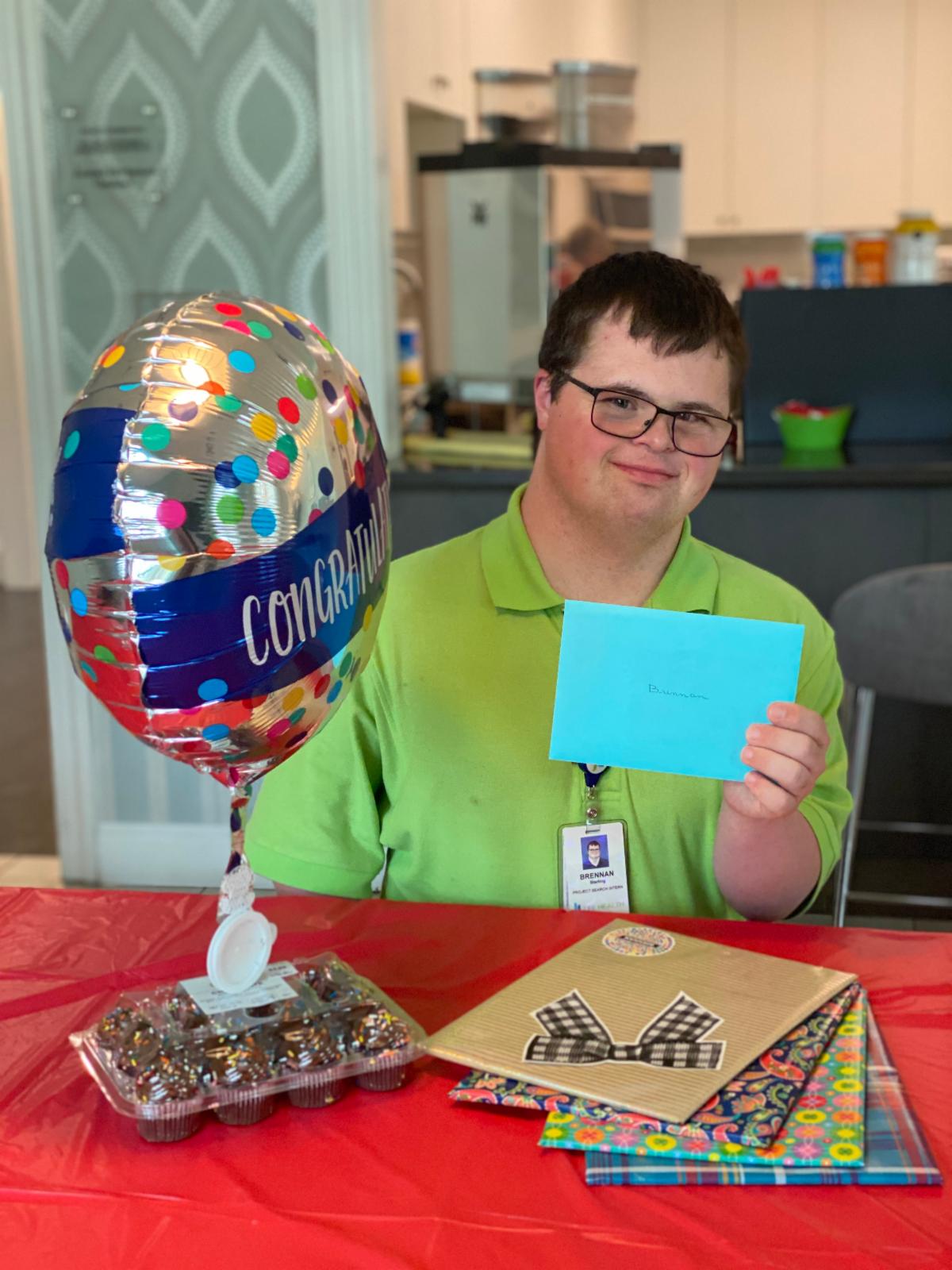 Smiling intern holds a card and balloon