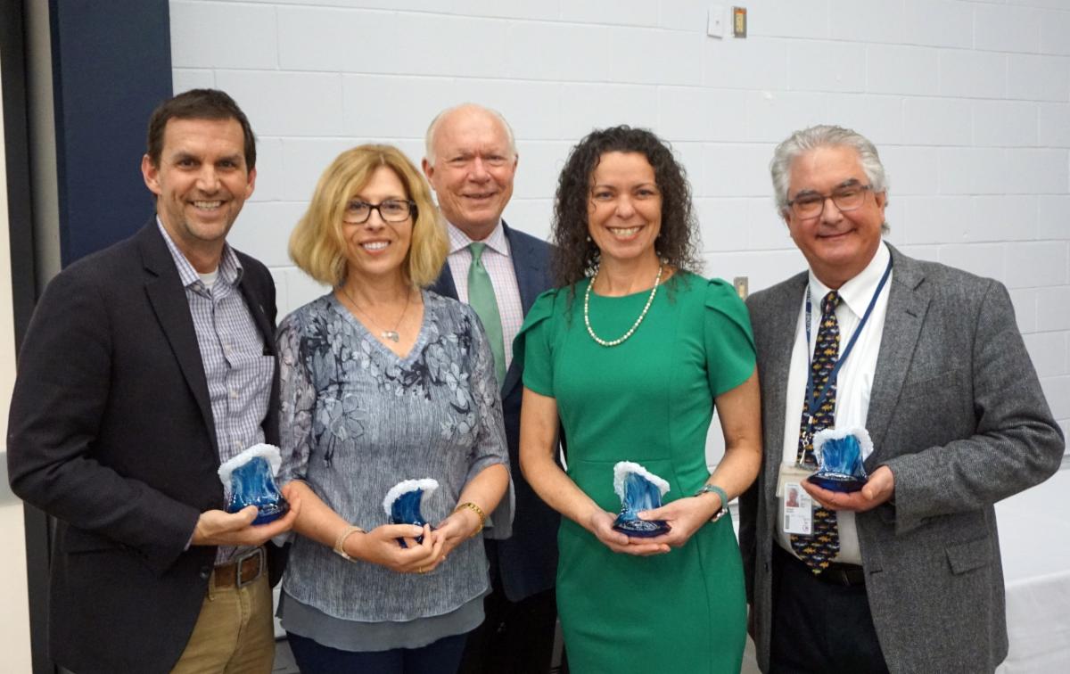 Four honorees holding blue glass wave awards.