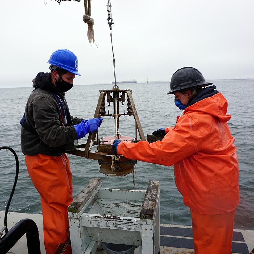 Students operate a sediment grab sampler aboard vessel.