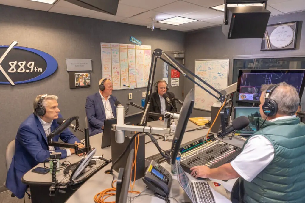 Four seated speakers conversing in a radio station room