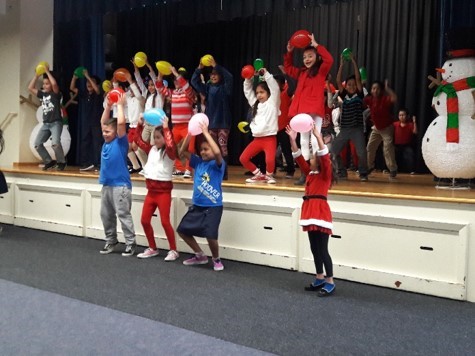 A pictures of a group of children on stage and on the ground holding balloons