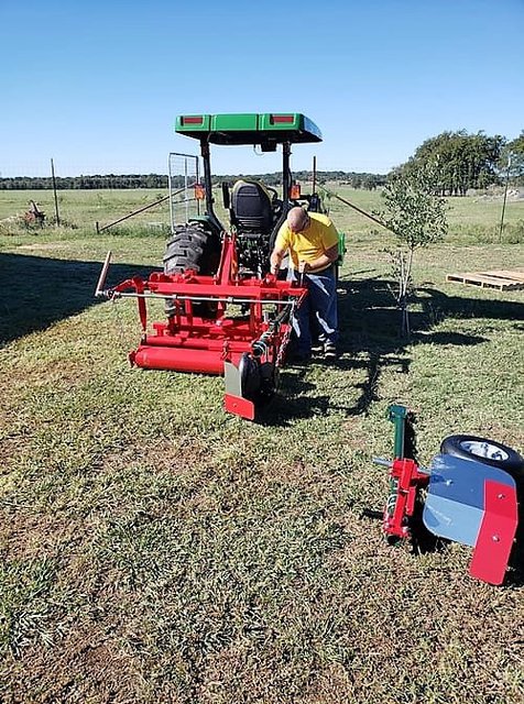 Damon Kleaton in a yellow shirt in a field working on his tractor with the red plastic mulch and irrigation layer attached