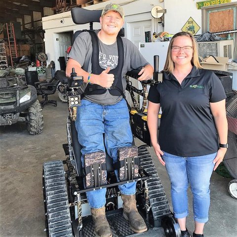 Rachel on right standing next to Cane who is standing with the aid of an Action Stander Trackchair 