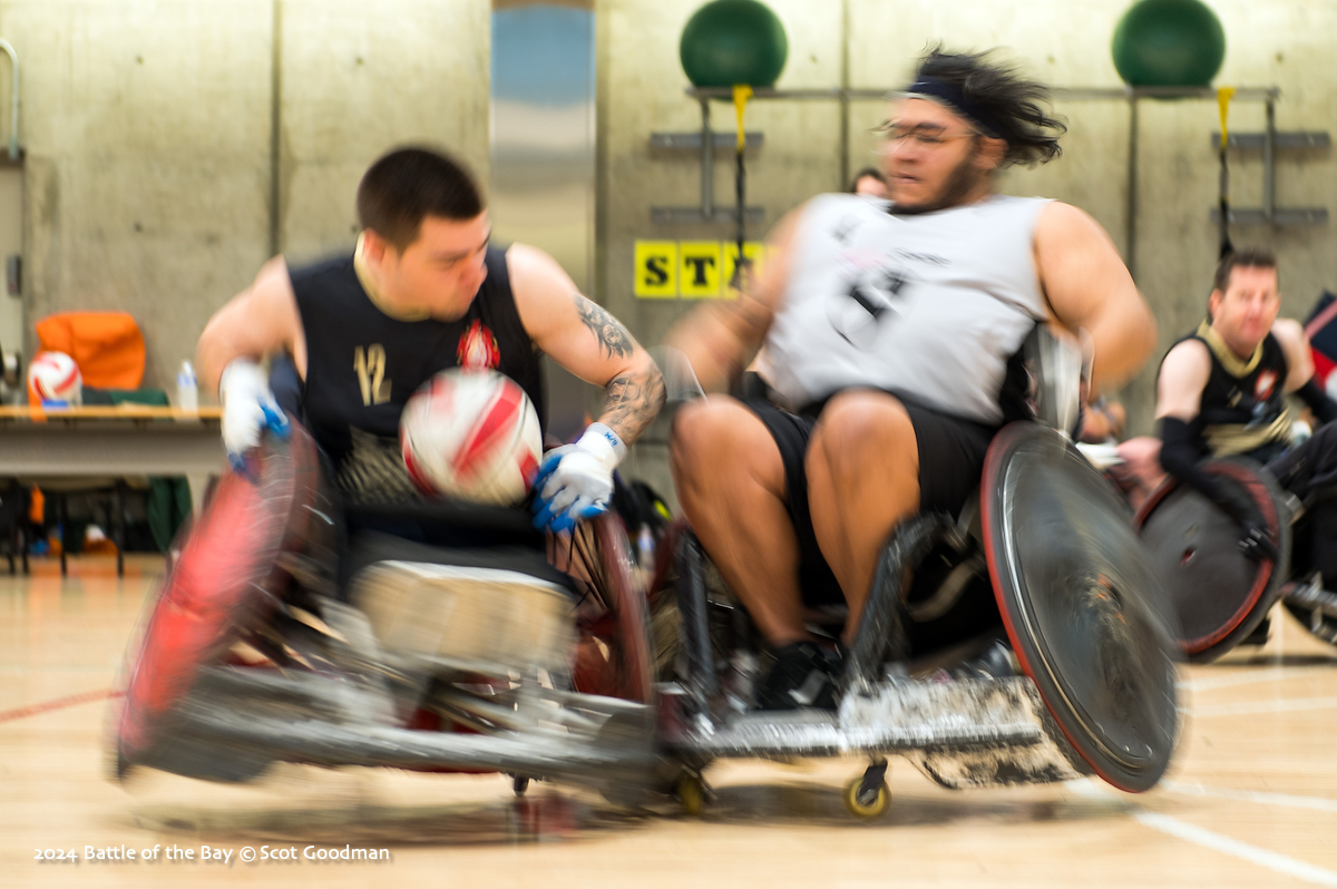 Photo of two men in rugby chairs (one with the ball) smashing into each other, blurred image of high velocity impact.