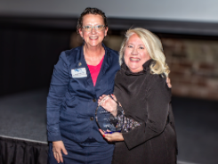 A woman is holding a trophy with another woman hugging her