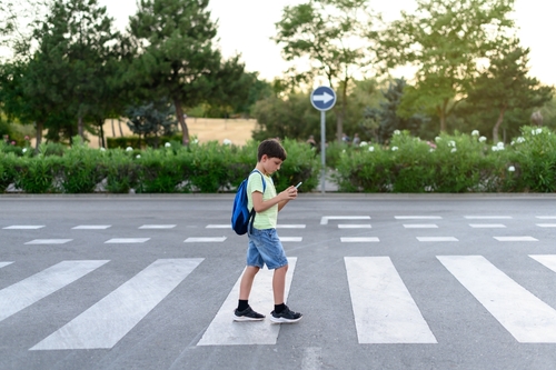 Boy looks at their mobile phones while crossing a crosswalk on the street. Concept of mobile phone addiction