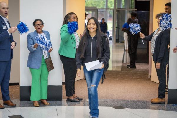 Early high school student entering building while staff wave pom poms