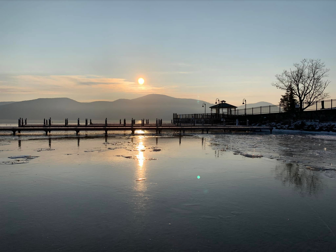 The sun shines through hazy clouds over a frozen Lake George. 