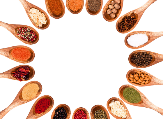 Assorted colorful spices and seasonings displayed in wooden spoons arranged in a circular border around a blank white center.