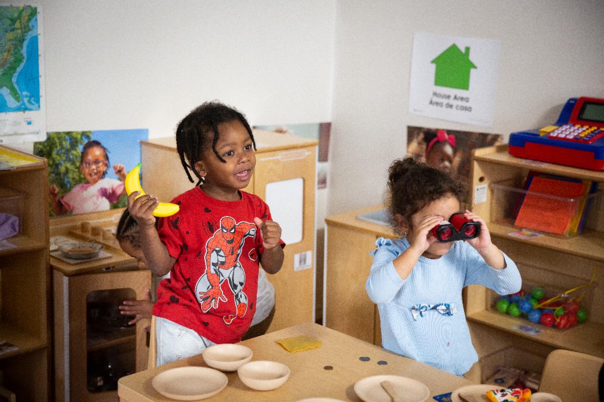 A child smiles next to another child looking through binoculars