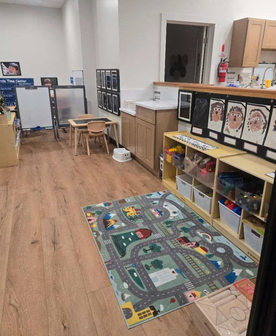 A preschool classroom with wooden shelves, bins of materials, a desk and chair, and children's artwork