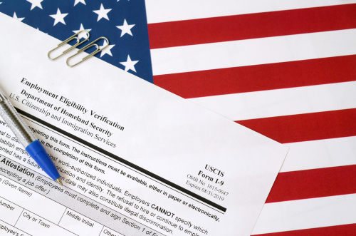 I-9 Employment Eligibility Verification blank form lies on United States flag with blue pen from Department of Homeland Security