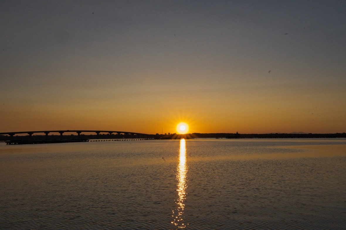 Sunrise over calm water, with golden light reflected toward the shore.