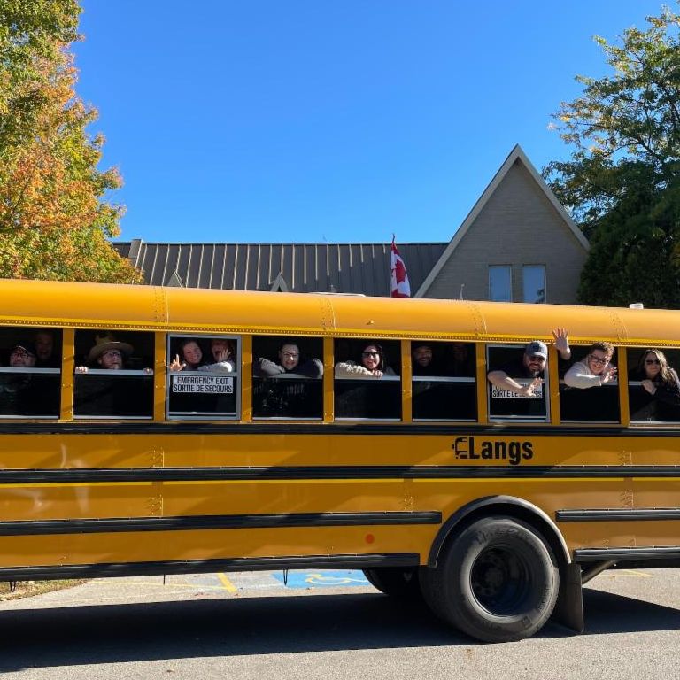 Side view of school bus with Destination Northern Ontario participants waving out the window