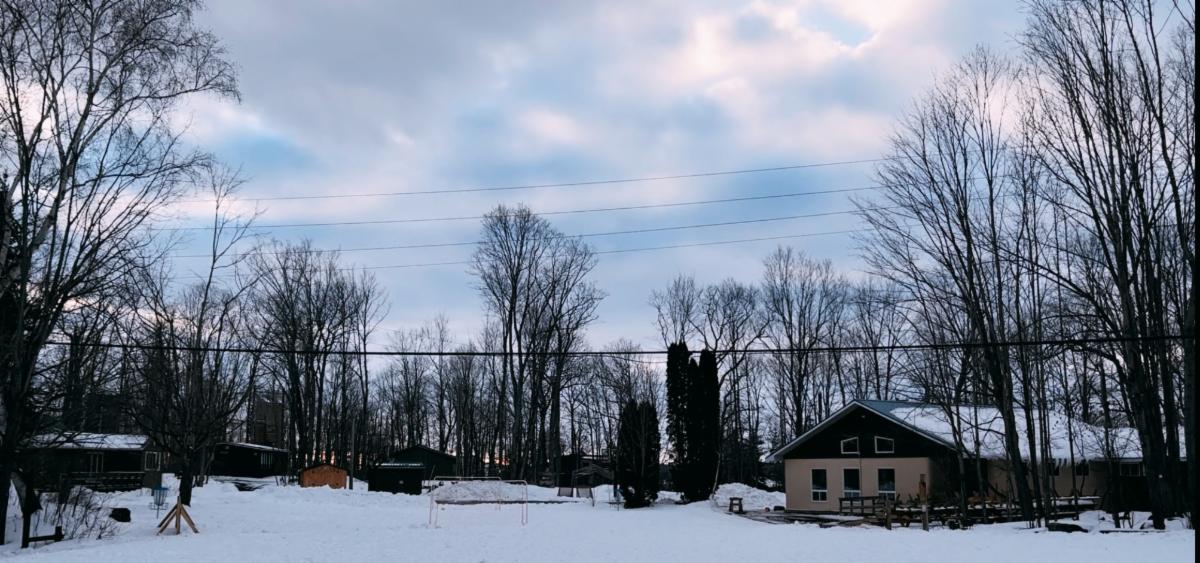 Upper playing field covered in snow at Camp Kawartha Rotary Hall on the far right of the image bare trees populate the background and there are a few cabins seen on the right