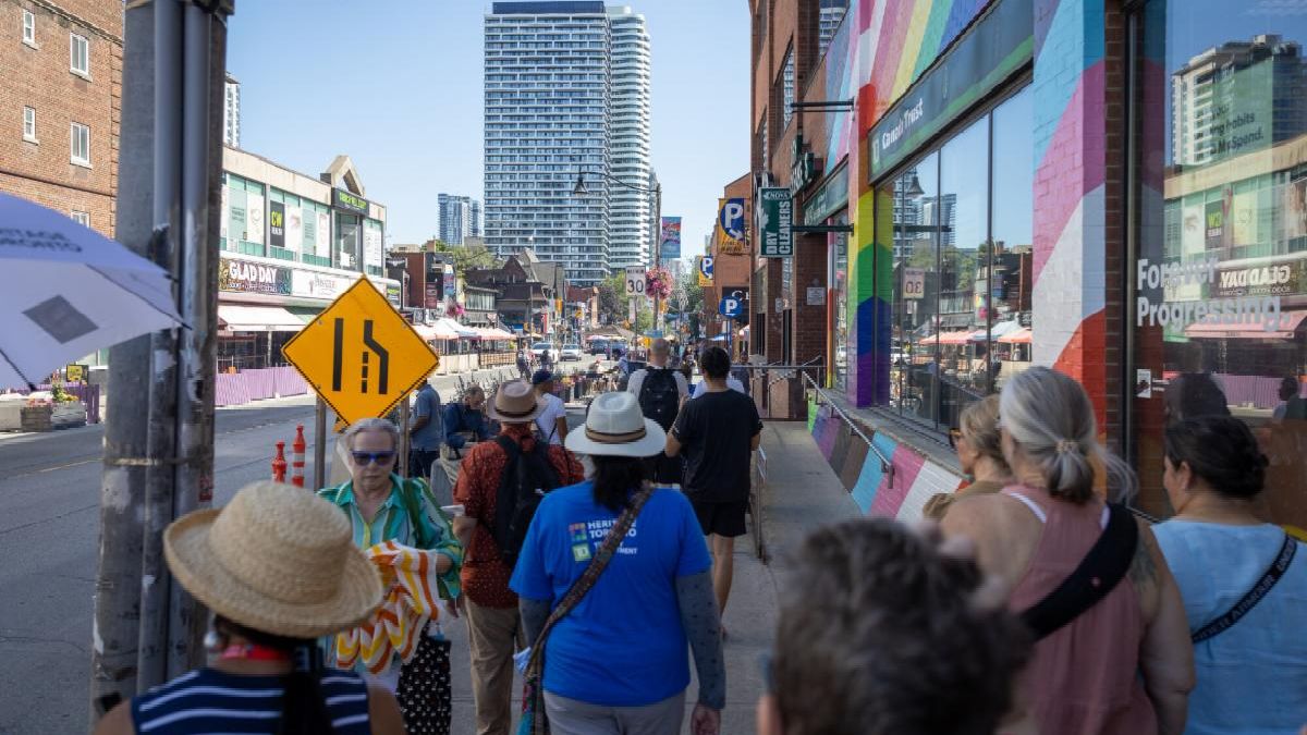 Group of people walk down a street. Brick walls on the right are painted in rainbow colours