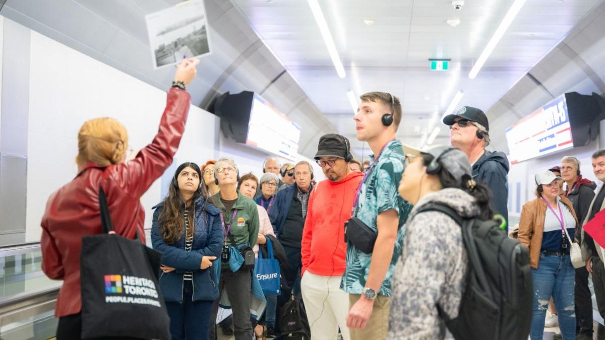 Group of people stand in a tunnel looking at a photo being held up by a person to the left.