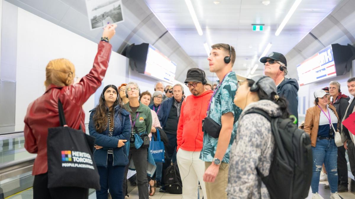 Group of people stand in a tunnel looking at a photo being held up by a person to the left.