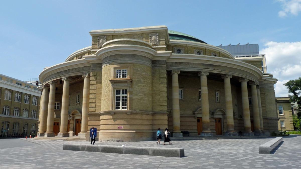 Large round yellow brick building with columns encompassing the structure on both sides.