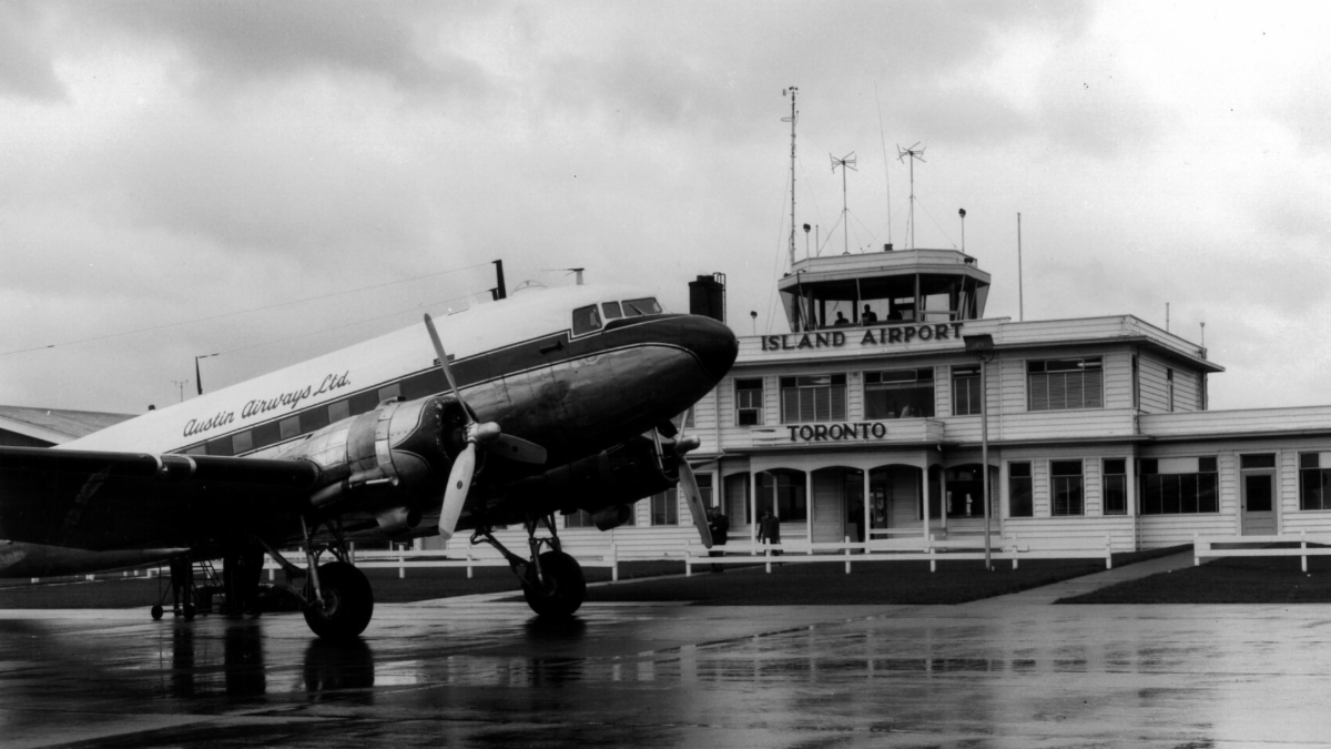 A black and white image of an airplane in front of a white building with the words Island Airport Toronto