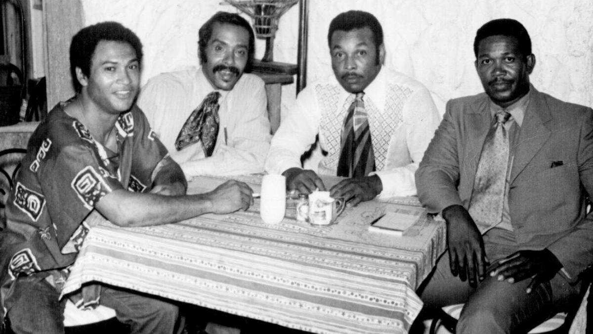 Image of four men seated at a small restaurant table posing for a photograph.
