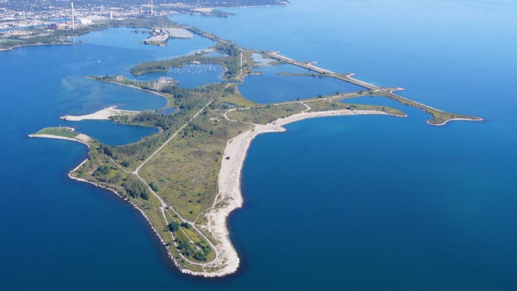 Colour aerial photo of a sinuous landform approximately 5 kilometres in length in a large body of water. It is connected to a mainland by a narrow neck of land.