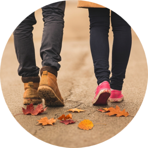 Two pairs of walking feet on a sidewalk with colorful fall leaves strewn around them