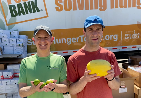 Dr. Devries and his son volunteering at a local food bank, smiling and holding limes and spaghetti squash to be given to food bank recipients.