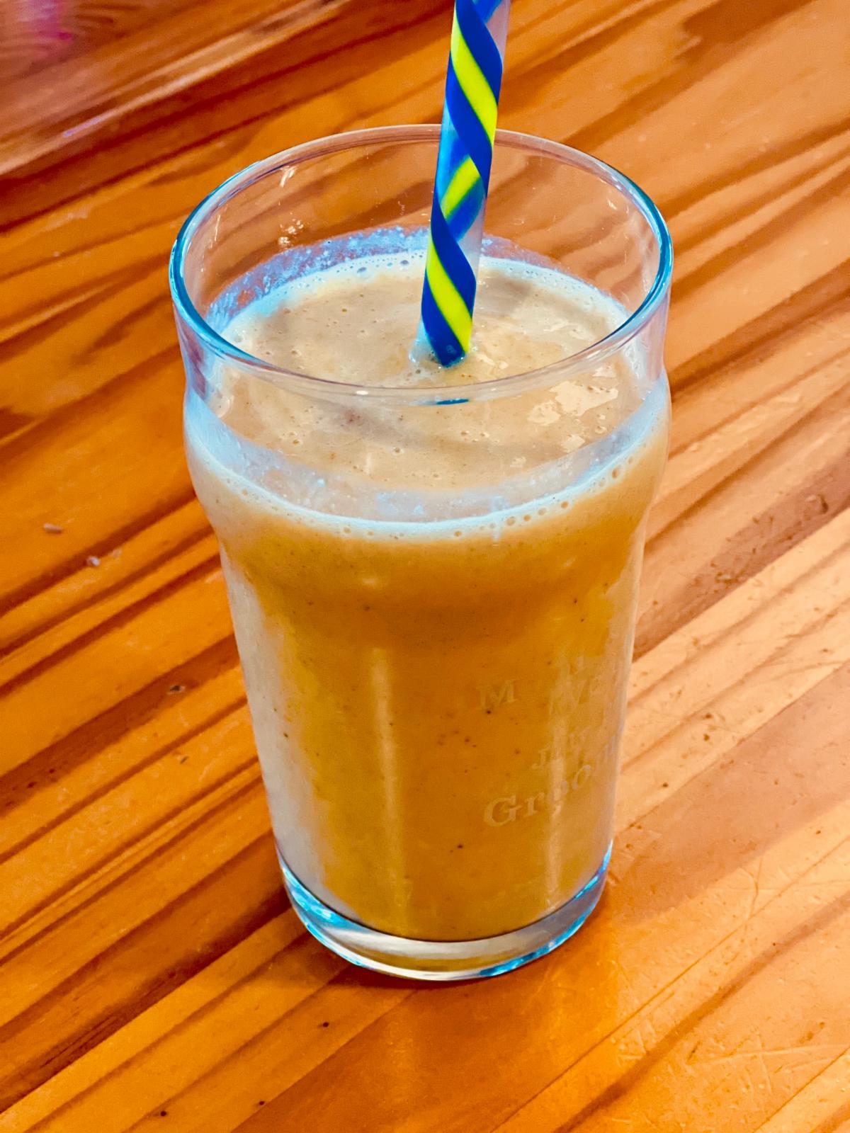 A glass filled with a bright orange creamy-looking drink, with a blue striped straw